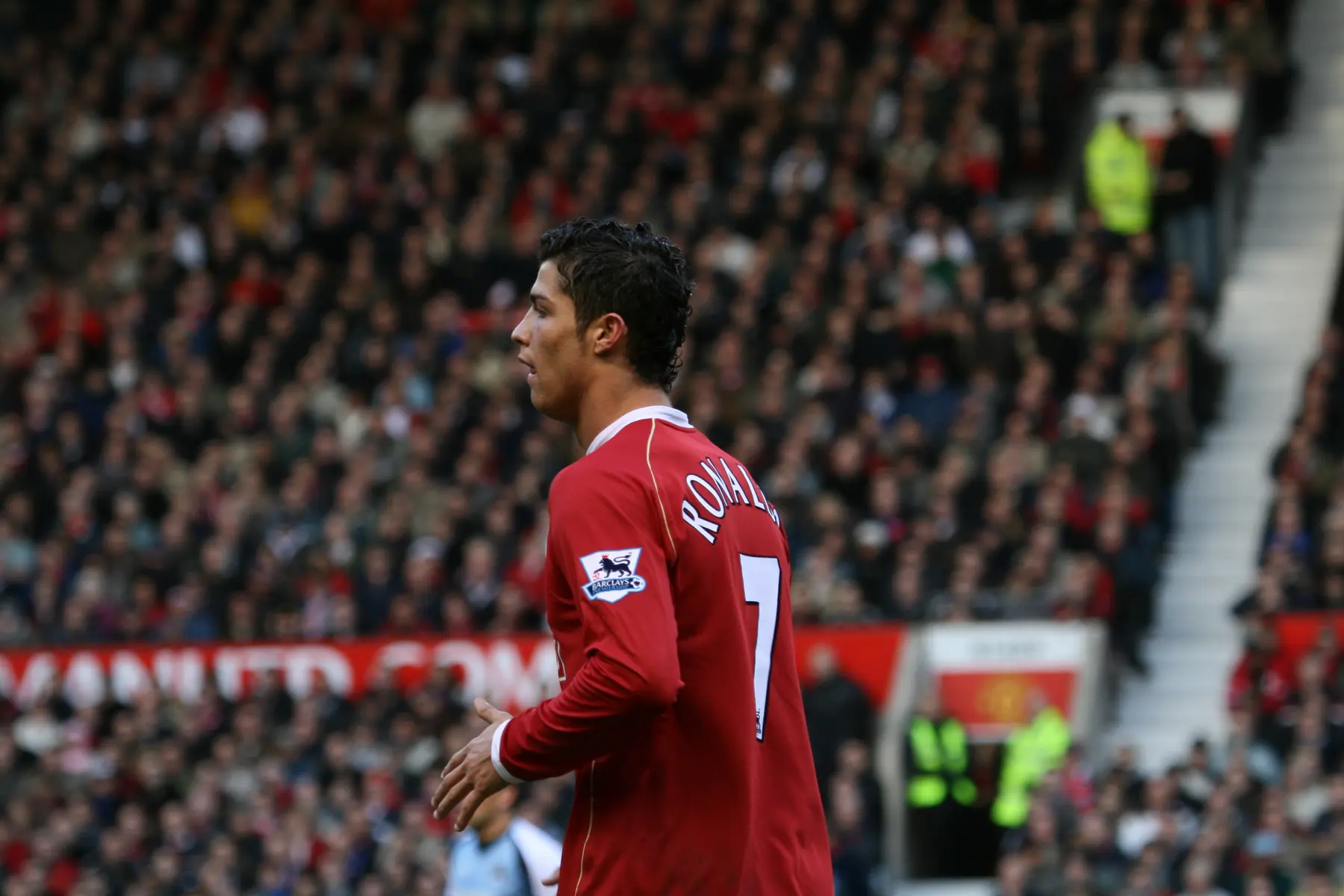 Cristiano Ronaldo vestindo a camisa vermelha do Manchester United em um campo de futebol com torcedores ao fundo.